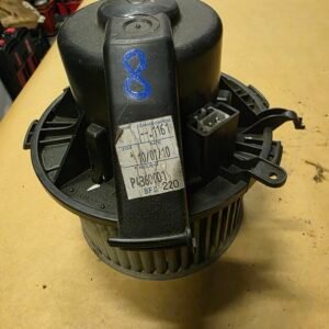 Black cylindrical automotive blower motor with a white label and a blue handwritten 8 on the side, on a wooden workbench.