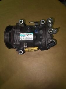 Automotive air conditioning compressor with drive pulley and mounting ports on a brown surface
