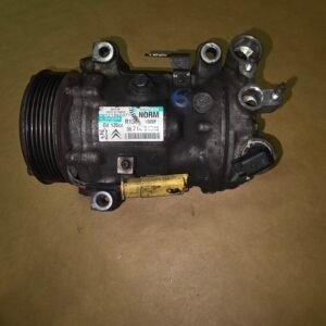 Automotive air conditioning compressor with drive pulley and mounting ports on a brown surface