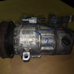 Dusty Renault automotive part with a large pulley (likely an AC compressor) and a metal label reading RENAU LT; appears worn and dirty on a brown surface.