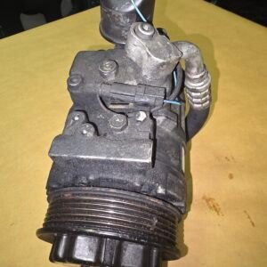 Automotive hydraulic pump assembly with a ribbed drive pulley at the bottom, hoses and a blue wire connected to the top.
