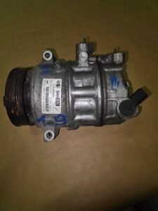 Automotive air conditioning compressor with a belt pulley on the left and mounting lugs on a brown background.